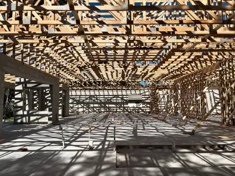 Sunlight cutting through a freshly set floor truss deck over the concrete slab of a commercial build