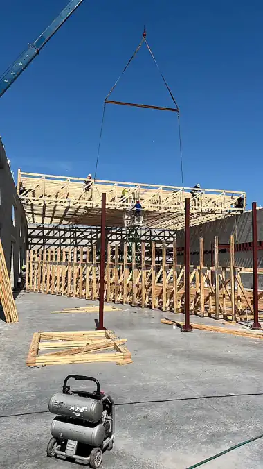 Crane spreader bar guiding a truss lift while the NBJJ crew works from the top plate of a block wall