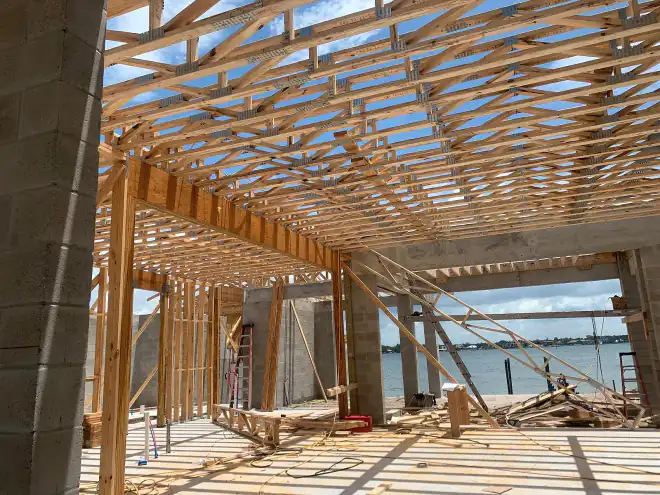 Open-web floor trusses overhead inside a waterfront build, water visible past the block walls