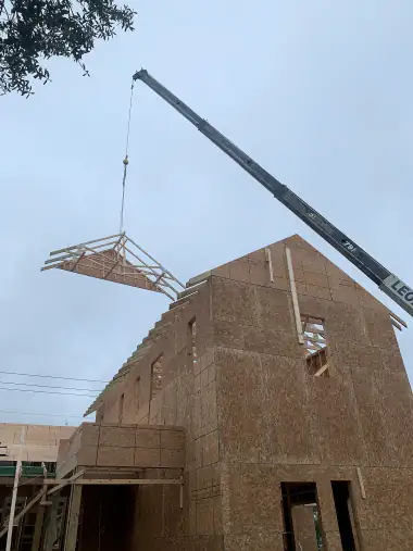 Crane hoisting a framed gable section into place against the sky on a Central Florida job