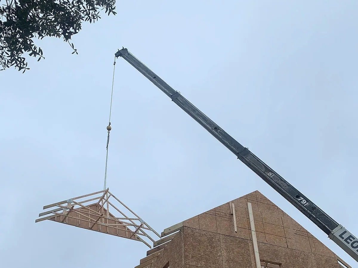 Crane lifting an engineered roof truss onto a sheathed gable wall